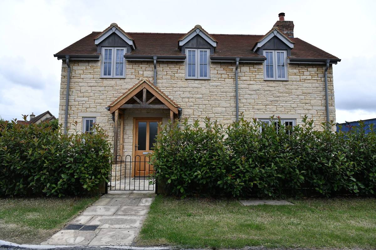 A recently built stone detached house with dormer windows, an oak porch and a laurel hedge